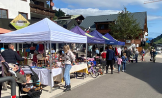 A busy market with several stalls and visitors. The atmosphere is friendly and there is a variety of products to see.