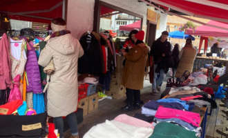 A lively market with several stalls offering clothing and accessories. People browse the offerings and enjoy the atmosphere.