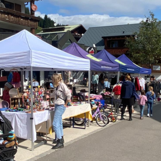 A busy market with several stalls and visitors. The atmosphere is friendly and there is a variety of products to see.