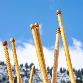 Eine Gruppe von Menschen spielt auf Alphörnern auf einer Terrasse. Im Hintergrund sind sonnige Berge und eine klare blaue Himmel zu sehen. | © Kleinwalsertal Tourismus | Frank Drechsel