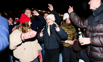 A group of people is joyfully celebrating at night. They are dancing and having fun while wearing various warm clothing.