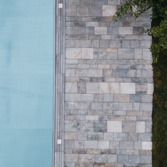Ein modern gestalteter Außenbereich mit einem blauen Pool und einem Steinweg. Rechts daneben liegt ein grüner Rasen und etwas Laub. | © Naturhotel Chesa Valisa