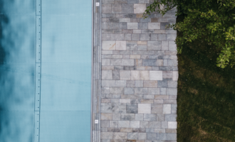 Ein modern gestalteter Außenbereich mit einem blauen Pool und einem Steinweg. Rechts daneben liegt ein grüner Rasen und etwas Laub. | © Naturhotel Chesa Valisa