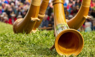 Three woodwind instruments lie on the grass. In the background, many people can be seen enjoying a celebration. | © Kleinwalsertal Tourismus | Frank Drechsel