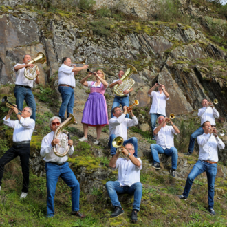 Eine Gruppe von Musikern steht auf einer grünen, bewachsenen Hügel, während sie verschiedene Blasinstrumente spielen. In der Mitte trägt eine Person ein lila Kleid und spielt mit Freude mit.