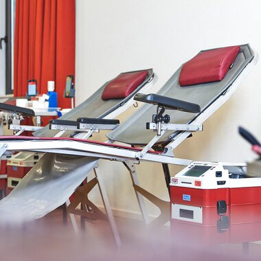 A room with two couches prepared for blood donations. In the background, additional equipment and a bright room with red curtains can be seen.