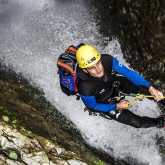 Ein Mann klettert an einer steilen Felswand in einem Wasserfall. Er trägt einen Helm und eine Kletterausrüstung. | © Bergschule Kleinwalsertal | Dominik Berchtold