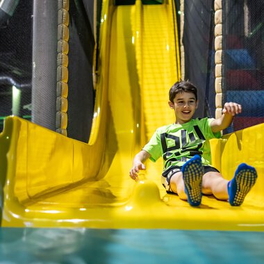 Ein fröhlicher Junge rutscht auf einer gelben Rutsche in einem Spielplatz. Der Raum ist bunt und einladend gestaltet. | © Wonnemar Sonthofen | interSPA Gruppe