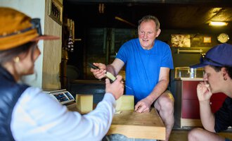 Ein Mann erklärt etwas, während zwei Personen aufmerksam zuhören. Die Szene spielt sich in einem rustikalen Innenraum ab. | © Kleinwalsertal Tourismus eGen - Fotograf: Oliver Farys