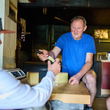 Ein Mann erklärt etwas, während zwei Personen aufmerksam zuhören. Die Szene spielt sich in einem rustikalen Innenraum ab. | © Kleinwalsertal Tourismus eGen - Fotograf: Oliver Farys