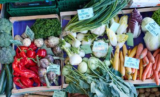 Ein bunter Markttisch mit frischem Gemüse. Es sind Paprika, Karotten, Kohlrabi und verschiedene Kräuter zu sehen. | © Kleinwalsertal Tourismus | Oliver Farys
