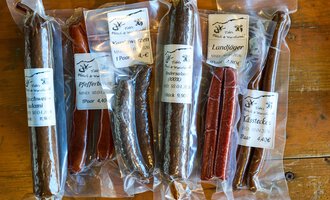 Auf dem Bild sind verschiedene Wurstsorten in durchsichtigen Verpackungen zu sehen. Die Würste sind farblich unterschiedlich und tragen Etiketten mit Produktinformationen.