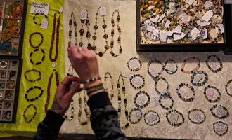 A display with various jewelry pieces made of pearls and stones. A person is looking at the necklaces and bracelets on a bright cloth.