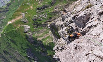 An impressive mountain landscape with steep cliffs and green meadows. A climber is on a rock face. | © stoamandl.at | Olli Sinz