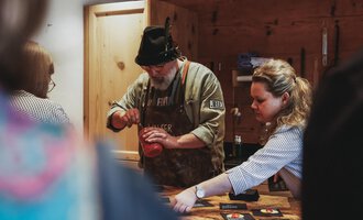 A man and a woman are preparing something in a cozy kitchen. The man is wearing a hat and an apron, while the woman is working intently. | © Angela Lamprecht | Vorarlberg Tourismus