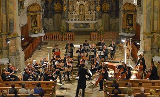 Ein Orchester spielt in einer Kirche, umgeben von kunstvollen Verzierungen. Das Publikum sitzt in den Bänken und lauscht der Musik. | © Collegium Instrumentale Stuttgart | Alfred Michel