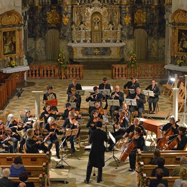 An orchestra plays in a church, surrounded by intricate decorations. The audience sits in the pews and listens to the music. | © Collegium Instrumentale Stuttgart