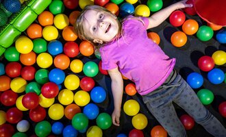 Ein glückliches Kind liegt in einem Ballpool mit bunten Bällen. Sie trägt ein lila T-Shirt und sieht entspannt aus. | © Wonnemar Sonthofen | interSPA Gruppe