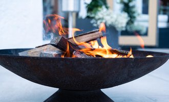 Ein rustikales Feuer in einem runden Feuerkorb. Die Flammen lodern über den Holzscheiten und schaffen eine gemütliche Atmosphäre. | © Genuss- & Aktivhotel Sonnenburg