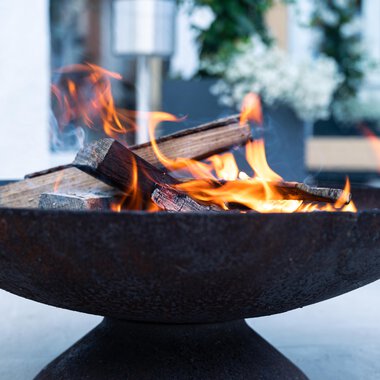 A rustic fire in a round fire pit. The flames flicker over the logs and create a cozy atmosphere. | © Genuss- & Aktivhotel Sonnenburg