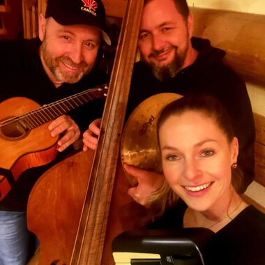 Three musicians pose together with their instruments in a warm, rustic room. They are smiling and seem to be having fun. | © Kulturcafe Kleinwalsertal | Matthias Zobel