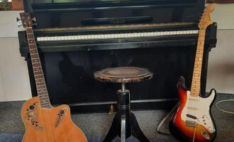 Ein Klavier steht im Hintergrund, flankiert von einer akustischen Gitarre links und einer E-Gitarre rechts. In der Mitte befindet sich ein Hocker. | © Kulturcafe Kleinwalsertal | Gerhard Bauer