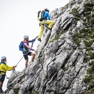 © Bergschule Kleinwalsertal | Dominik Berchtold Drei Kletterer erklimmen einen steilen Felsen. Sie tragen Helme und Kletterausrüstung, während sie sich sicher an Seilen festhalten. | © Bergschule Kleinwalsertal | Dominik Berchtold