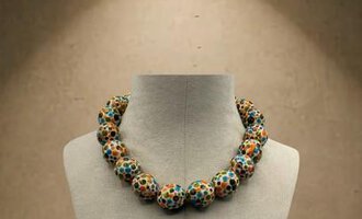 A striking necklace with colorful beads lies on a display window. The gentle lighting accentuates the piece of jewelry.