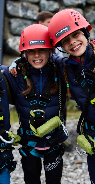 Drei fröhliche Kinder in Kletterhelmen und Sicherheitsgeschirren lächeln in die Kamera. Sie sind bereit für ein aufregendes Abenteuer in der Natur. | © Kleinwalsertal Tourismus | Oliver Farys