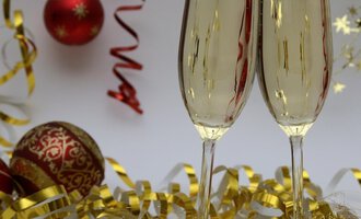 Two champagne glasses toast on a festively decorated table. In the background, red Christmas ornaments and golden decorations can be seen. | © Genuss- & Aktivhotel Sonnenburg