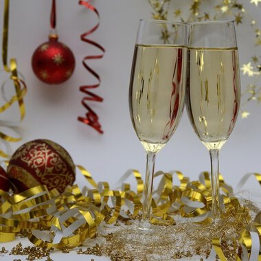 Two champagne glasses toast on a festively decorated table. In the background, red Christmas ornaments and golden decorations can be seen. | © Genuss- & Aktivhotel Sonnenburg
