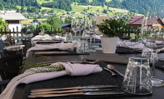 Ein schön gedeckter Tisch auf einer Terrasse mit Blick auf grüne Hügel. Sonnenschirme spenden Schatten für die Gäste. | © Genuss- & Aktivhotel Sonnenburg