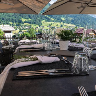 A beautifully set table on a terrace overlooking green hills. Umbrellas provide shade for the guests. | © Genuss- & Aktivhotel Sonnenburg