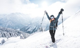 A skier in a blue suit is skiing through fresh, powdery snow. In the background, snow-covered mountains and a clear blue sky can be seen.