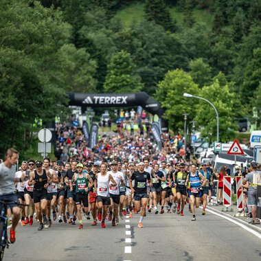 A large running event with many participants starting on a street. In the background, trees and a starting line are visible. | © Kleinwalsertal Tourismus - Dominik Berchtold