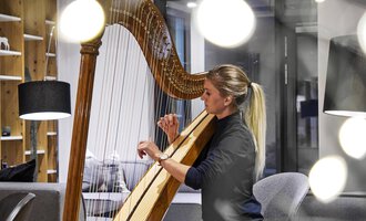 A woman is playing the harp in a modern room. Soft light and stylish furniture create a cozy atmosphere. | © Genuss- & Aktivhotel Sonnenburg | Michael Gunz