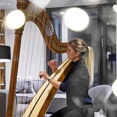 A woman is playing the harp in a modern room. Soft light and stylish furniture create a cozy atmosphere. | © Genuss- & Aktivhotel Sonnenburg | Michael Gunz