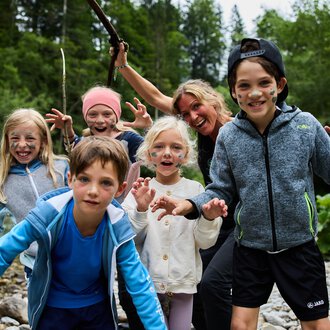 A group of children and an adult standing at the riverbank. They are having fun and posing with happy facial expressions. | © Kleinwalsertal Tourismus | Oliver Farys