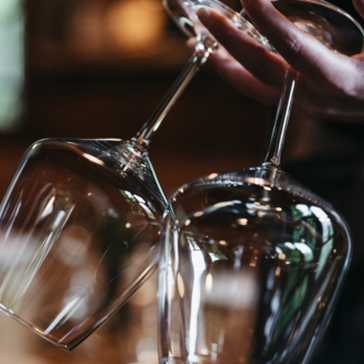 Eine Person hält zwei elegante Weingläser. Der Hintergrund ist verschwommen und erzeugt eine gemütliche Atmosphäre. | © Winzer zu Tisch | Naturhotel Chesa Valisa