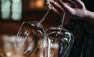 Eine Person hält zwei elegante Weingläser. Der Hintergrund ist verschwommen und erzeugt eine gemütliche Atmosphäre. | © Winzer zu Tisch | Naturhotel Chesa Valisa