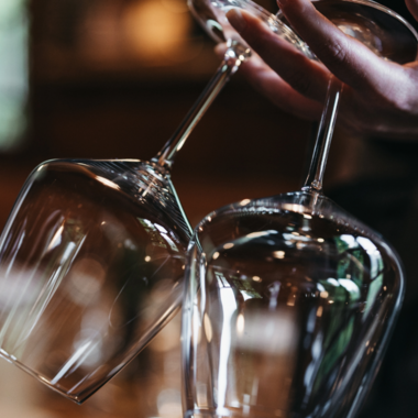 Eine Person hält zwei elegante Weingläser. Der Hintergrund ist verschwommen und erzeugt eine gemütliche Atmosphäre. | © Winzer zu Tisch | Naturhotel Chesa Valisa