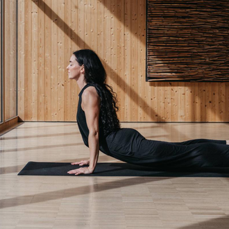 Ein heller Yogaraum mit Holzverkleidung und großen Fenstern. Drei Personen praktizieren Yoga und blicken nach draußen. | © Naturhotel Chesa Valisa