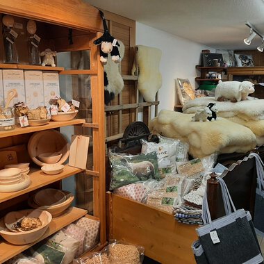Ein gemütlicher Laden mit Holzregalen voller Handwerksprodukte. Im Hintergrund liegen hochwertige Wollprodukte und Dekorationen. | © Abler Mitbringsel Riezlern | Veronika Senn