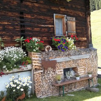 A traditional wooden house with colorful flowers and wood piles. The place radiates rural coziness and a connection to nature. | © Kleinwalsertal Tourismus | N. Lughammer