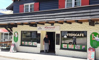 A traditional restaurant with an inviting entrance and a terrace. The facade is designed in light and dark colors, with a small group of menus and offers on posters. | © Alpengrill Riezlern | Veronika Senn