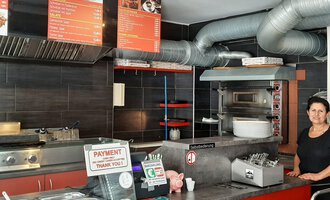 An inviting restaurant with an open kitchen and a friendly atmosphere. In the background, the menus and various kitchen utensils can be seen. | © Alpengrill Riezlern | Veronika Senn