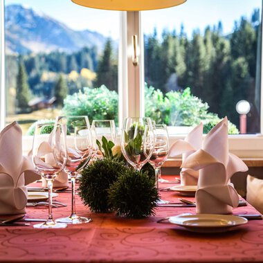 Ein schön gedeckter Tisch mit Gläsern und gefalteten Servietten. Im Hintergrund sieht man eine Aussicht auf Berge und Bäume. | © Alpenhotel DAS KÜREN