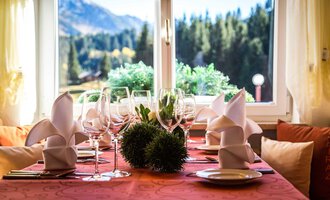 Ein schön gedeckter Tisch mit Gläsern und gefalteten Servietten. Im Hintergrund sieht man eine Aussicht auf Berge und Bäume. | © Alpenhotel DAS KÜREN