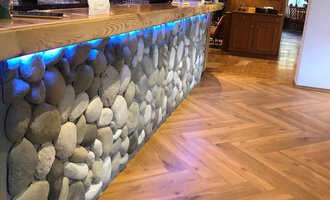 Eine stilvolle Bar mit einem Steinelement und einer beleuchteten Holzoberfläche. Der Fußboden besteht aus einem attraktiven Fischgrätmuster.