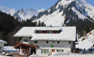 Ein malerisches Hotel in den Alpen, umgeben von schneebedeckten Bergen. Die Landschaft ist winterlich und einladend.
